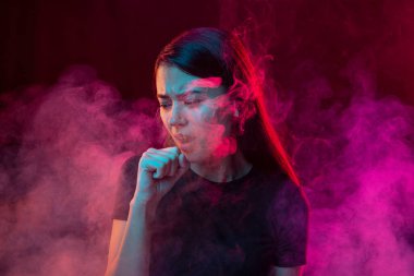 Smokers cough. Sick young man with stressed emotions isolated over dark pink background with clouds of smoke in neon. Concept of health, addiction, human emotions, challenges, ad