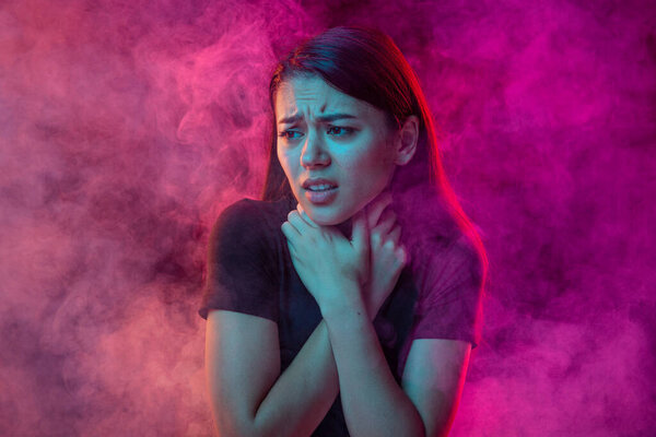 Suffocate in the smoke. Scared young man with stressed emotions isolated over pink background with clouds of smoke. Concept of mental health, art, human emotions, challenges, ad