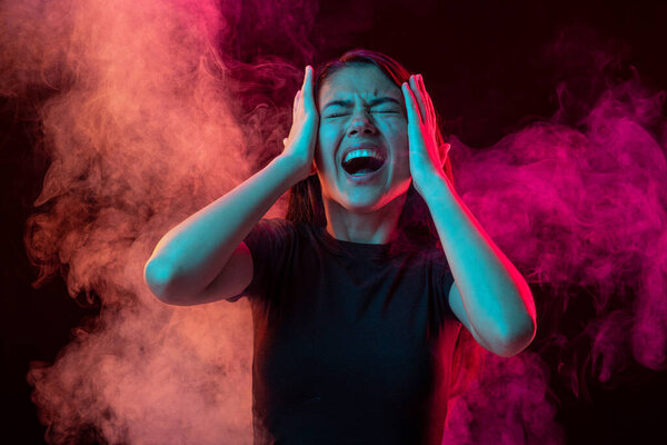 Emotional pain. Young dark hair woman shouting isolated over pink background with clouds of smoke. Concept of mental health, art, human emotions, challenges, ad