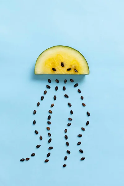 Dancing cloud. Creative design with slice of yellow mango or pineapple watermelon with seeds raining isolated over blue background. Flat lay. Weather concept. Art, taste, health, ad