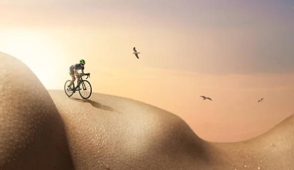 Sunset at desert. Young athlete-cyclist rides on surface of female body against background of natural landscape with evening sky with sun rays. Skincare, inspiration, fantasy