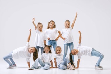 Modern choreography, synchronized movements. Active little girls, sportive kids in casual style clothes in motion isolated on white studio background. Concept of music, fashion, art, childhood, hobby.