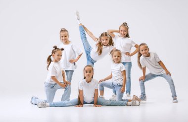 Joy, fun and happiness. Portrait of happy, active little girls, sportive kids in casual clothes dancing isolated on white studio background. Concept of music, fashion, art, childhood, hobby.