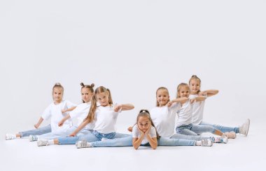 Modern choreography, synchronized movements. Active little girls, sportive kids in casual style clothes in motion isolated on white studio background. Concept of music, fashion, art, childhood, hobby.