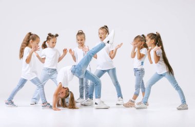 Joy, fun and happiness. Portrait of happy, active little girls, sportive kids in casual clothes dancing isolated on white studio background. Concept of music, fashion, art, childhood, hobby.