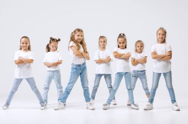 Modern choreography lesson. Dance group of happy, active little girls in jeans and t-shirts dancing isolated on white studio background. Concept of music, fashion, art, childhood, hobby.