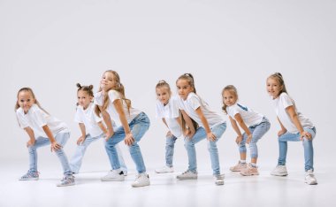 Joy, fun and happiness. Portrait of happy, active little girls, sportive kids in casual clothes dancing isolated on white studio background. Concept of music, fashion, art, childhood, hobby.