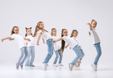 Modern choreography lesson. Dance group of happy, active little girls in jeans and t-shirts dancing isolated on white studio background. Concept of music, fashion, art, childhood, hobby.