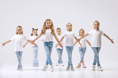 Modern choreography lesson. Dance group of happy, active little girls in jeans and t-shirts dancing isolated on white studio background. Concept of music, fashion, art, childhood, hobby.