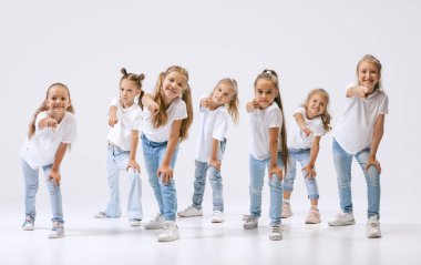 Joy, fun and happiness. Portrait of happy, active little girls, sportive kids in casual clothes dancing isolated on white studio background. Concept of music, fashion, art, childhood, hobby.