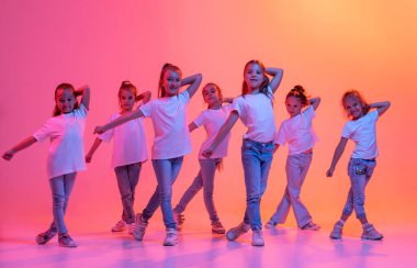 Hip-hop dance, street style. Group of children, school age girls in casual style clothes dancing in choreography class isolated on pink background in yellow neon light. Concept of music, fashion, art