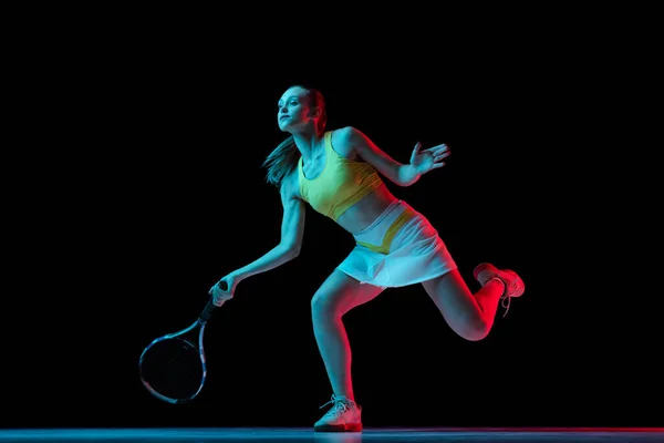 Champion. Young woman, professional tennis player training isolated on blue background in neon. Healthy lifestyle. The practicing, fitness, sport concept. The female model in motion or movement