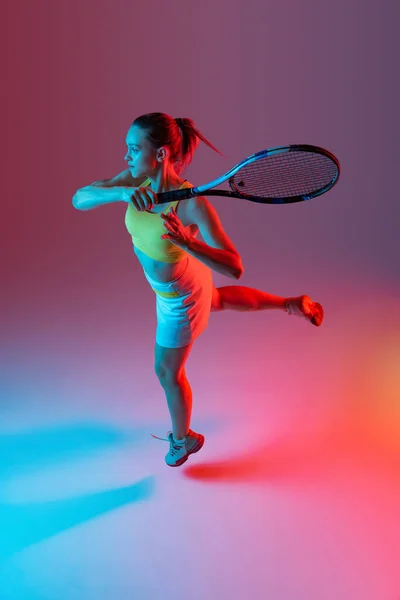 Aerial view. Training of female tennis player practicing power serving isolated on dark background in neon. Sports emotions, healthy lifestyle, fitness, sport, achievements concept.