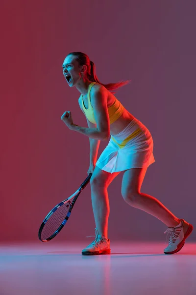 Winner emotions. Excited young woman, tennis player shouting after sports win isolated on purple background in neon. Healthy lifestyle, fitness, sport, exercise concept.