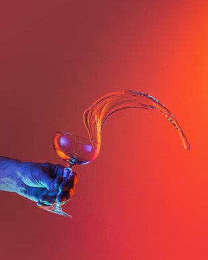 Imagination. Male hand pouring clean fluid from cocktail glass over bright dark red background in neon light. Concept of art, beauty, fashion, drinks, creativity. Copy space for ad