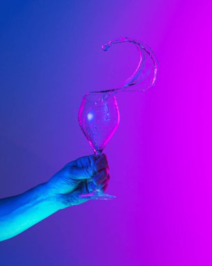 Flying fluid. Authentic hand pouring pure water splash from wine or champagne glass over bright blue-pink gradient background in neon light. Art, drinks, creativity