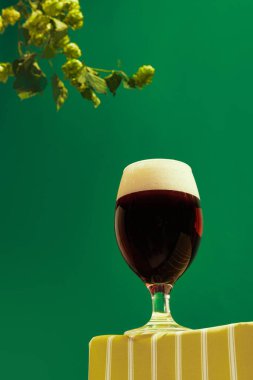 Autumn vibes. Glass of cold frothy dark beer over dark green background with hop cones. Oktoberfest, vacation, happiness, drinks, travel, fest and ad concept. Retro style.