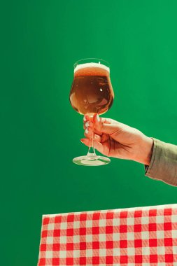Tasting beer. Female hand holding glass of cold dark beer over dark green background. Oktoberfest, vacation, happiness, drinks, Bavaria, travel, fest and ad concept. Retro style.