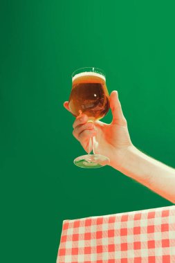 Tasting beer. Female hand holding glass of cold dark beer over dark green background. Oktoberfest, vacation, happiness, drinks, Bavaria, travel, fest and ad concept. Retro style.
