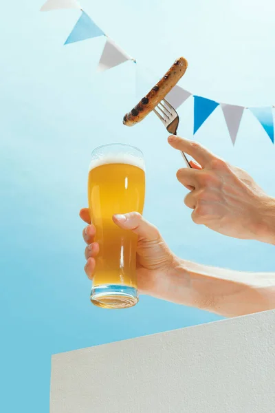 Drinks and snacks. Male hand with glass, mug of cold light beer over light blue sky background. Oktoberfest, vacation, happiness, drinks, beach, travel, fest and ad concept. Retro style.