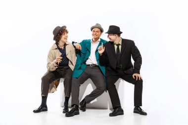 Group of young men in 70s, 80s fashion style clothes sitting and talking isolated on white background. Concept of culture, art, retro vintage style, ad