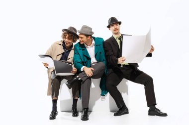 Reading latest news. Group of young men in 70s, 80s fashion style clothes posing isolated on white background. Concept of culture, art, music, style, ad