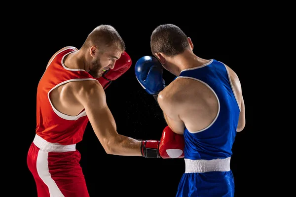 Training. Young men, professional boxers in red and blue sports uniform boxing isolated on dark background. Concept of sport, skills, power, training, energy. Copy space for ad, text