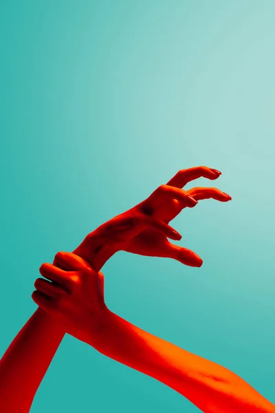 Stop agression. Female hands gesturing isolated on cyan color background in red neon light. Concept of relationship, community, care, support, symbolism, culture. Copy space for ad