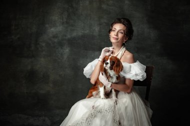 Charm and grace. Vintage portrait of young elegant woman in image of medieval person in renaissance style dress isolated on dark background. Comparison of eras, beauty, history, art, creativity.