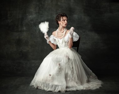 Temptation. Young adorable girl in image of medieval royal person or viscountess tasting sweets isolated on dark vintage background. Comparison of eras concept, fashion, art, ad.