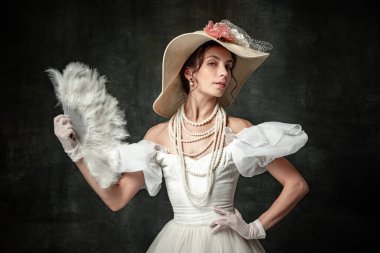 Charm. Creative portrait of young beautiful girl elegant dress of medieval fashion style with veer isolated on dark background. Comparison of eras concept, flemish style. Classic art character, old