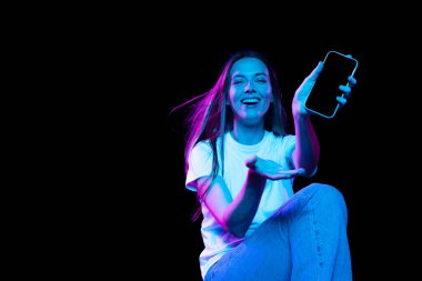 Beautiful emotional girl inviting for shopping, black friday, seasonal sales isolated over dark background in neon light. Cyber monday and online purchases. Art, fashion, emotions, ad