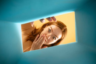 Beautiful young exressive girl opening, unpacking carton box and looking inside. Delivery, surprise, gift, wow emotions concept. Black friday, holidays, online shopping