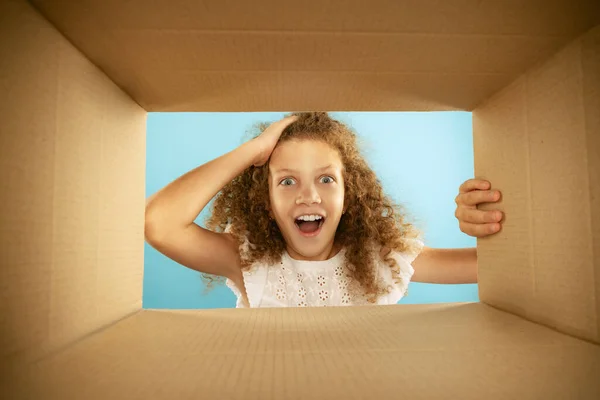 Happiness, delight. Emotional kid, little girl looking inside box during opening, unpacking it. Delivery, surprise, gift, wow emotions concept. Black friday, holidays and online shopping