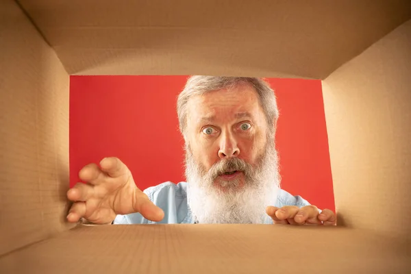Wonder. Senior bearded man unpacking, opening carton box and looking inside. Delivery, surprise, gift, wow emotions concept. Black friday, holidays, online shopping