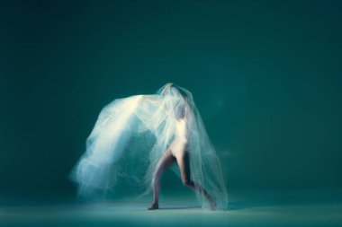 Fantasy. Creative portrait of flexible ballet dancer in motion with white cloth, fabric isolated on green blue background. Art, beauty, creation, inspiration concept. Blurring effect