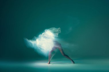 Ghostly vision. Tender girl, ballet dancer dancing with white cloth isolated on green background. Art, beauty, aspiration, flexibility, inspiration concept. Blurring effect, mixed light