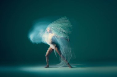 Freedom. Beautiful and graceful ballet dancer dancing with white transparent cloth, isolated on cyan color background. Concept of art, action, flexibility and inspiration concept. Blurring effect