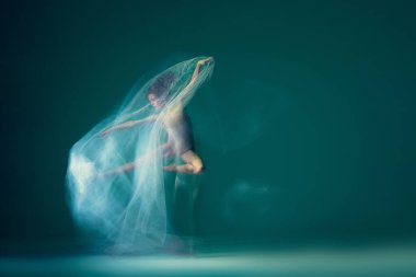 Jump and hover while in air. Creative portrait of flexible ballet dancer in motion with white cloth isolated on green blue background. Art, beauty, creation, inspiration concept. Blurring effect
