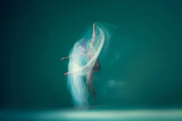Solo performance. Beautiful ballet dancer dancing with white transparent cloth, isolated on cyan color background. Concept of art, motion, action, flexibility and inspiration concept. Blurring effect