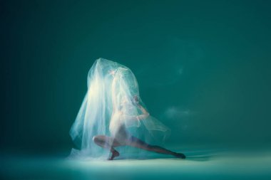 Ghostly vision. Tender girl, ballet dancer dancing with white cloth isolated on green background. Art, beauty, aspiration, flexibility, inspiration concept. Blurring effect, mixed light