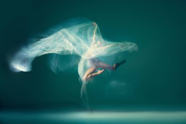 Jump and hover while in air. Portrait of flexible ballet dancer in motion with white cloth, fabric isolated on green blue background. Art, beauty, creation, inspiration concept. Blurring effect