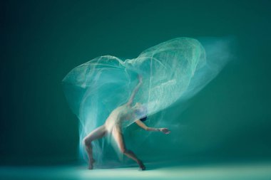 Under invisible pressure. Flexible ballet dancer dancing with white transparent fabric isolated on green background. Concept of art, action, flexibility and inspiration concept. Blurring effect