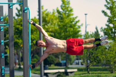 Workout. Strong muscular man, student training, practicing at sport ground at public park in summer morning, outdoors. Action, skills, challenges and achievements concept