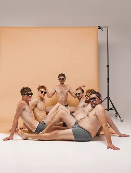 Dudes. Team of young handsome men of different body types sitting together in underwear on floor at studio photo shoot. Fun, joy, body positive and emotions Model having fun