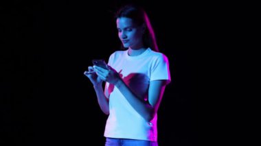 Young excited girl scrolling phone screen and shouting with delight isolated over dark background in neon light. Concept of business, black friday sales, ad, discount, cyber monday, online purchases.