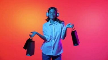 Fashionable happy young girl dancing with shopping packages, bags isolated over magenta background in yellow neon light. Concept of business, black friday sales, ad, discount, cyber monday