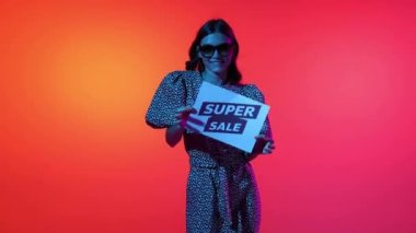 News, announcement. Joyful beautiful girl holding paper sign with lettering super sale, smiling and dancing. Concept of business, black friday sales, ad, discount, cyber monday