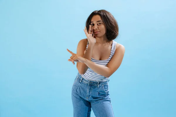 Whisper. Half-length portrait of young girl, student wearing casual style clothes isolated on blue background. Concept of beauty, art, fashion, youth, sales and ad, education, studying.