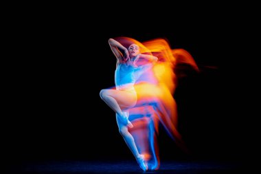Dynamic portrait of tender slim girl, female ballet dancer in art performance isolated over black background in mixed bright neon light. Art, motion, action, flexibility, creativity and ad concept.
